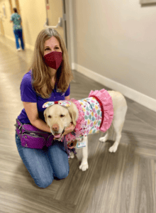 Therapy Dog team, Laura kneeling with her dog Gracie dressed up in a pink tutu dress.